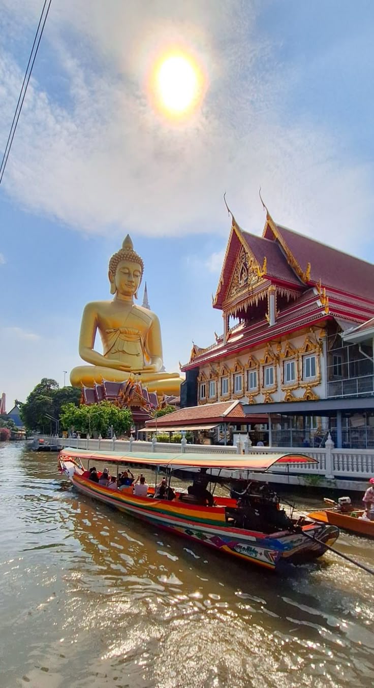Colourful long-tail boat on the river with a giant golden Buddha and temple in Thailand